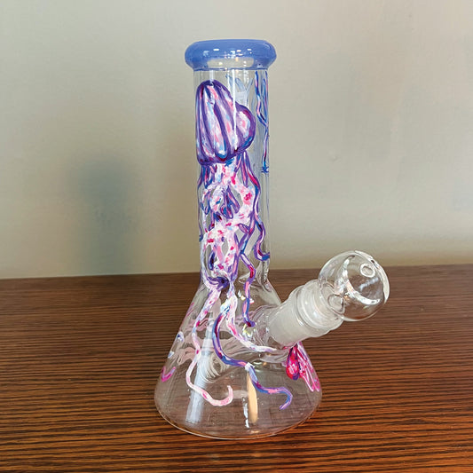 This is a hand painted beaker bong. The bong is painted with jellyfish. In this angle of the bong there is a jellyfish towards the top is purple with accents of pink and blue.