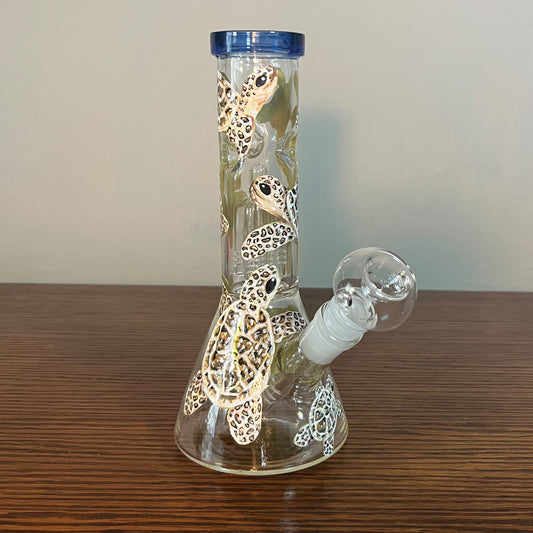 This is an 8 in beaker bong that is hand painted with little turtles swimming all over it. the turtles are different shades of brown. The top rim of the bong is a dark blue stained glass and the bowl is circular.